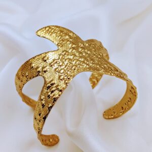 Close-up of a gold-toned textured cuff bracelet by Jhunkaar on a white satin background.