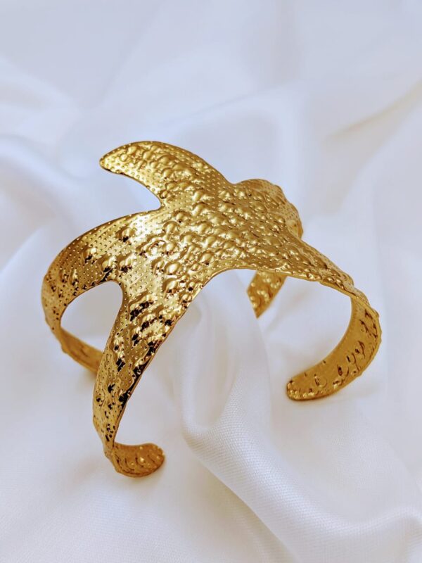 Close-up of a gold-toned textured cuff bracelet by Jhunkaar on a white satin background.