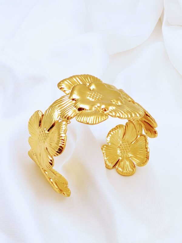 Golden flower cuff bracelet by Jhunkaar on a white satin background.