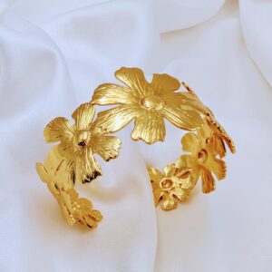 Jhunkaar golden floral cuff bracelet on a white silk background.