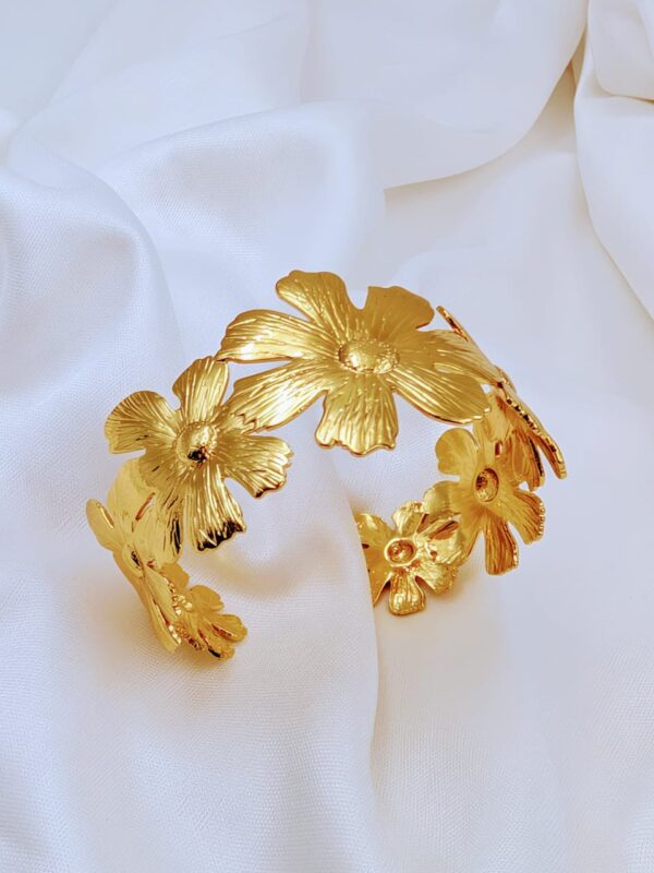 Jhunkaar golden floral cuff bracelet on a white silk background.