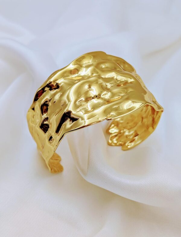 Jhunkaar textured gold bracelet on a white silk background.