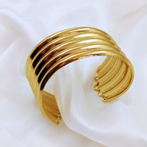 Jhunkaar gold cuff bracelet with a ribbed design on a white silk background.