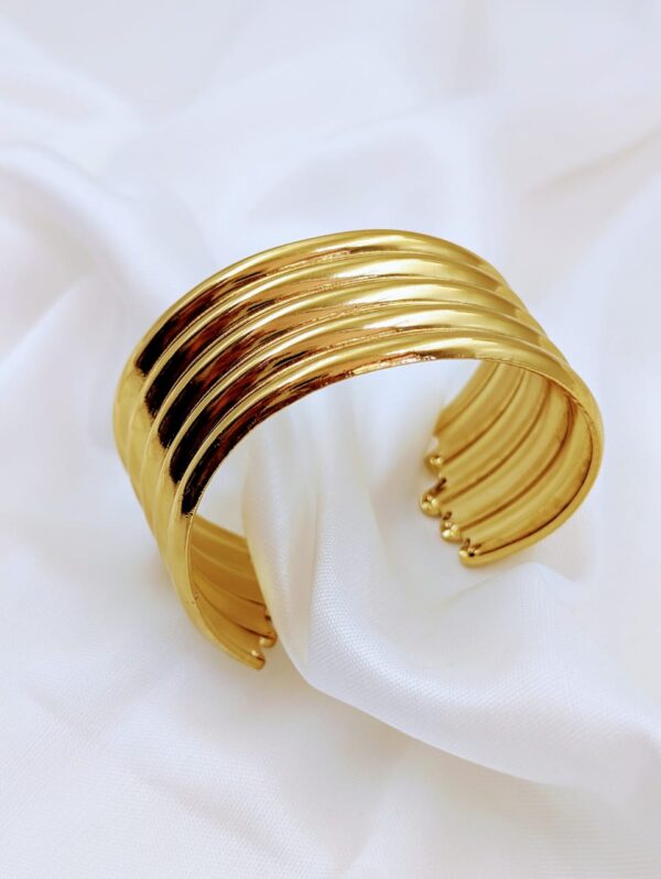 Jhunkaar gold cuff bracelet with a ribbed design on a white silk background.