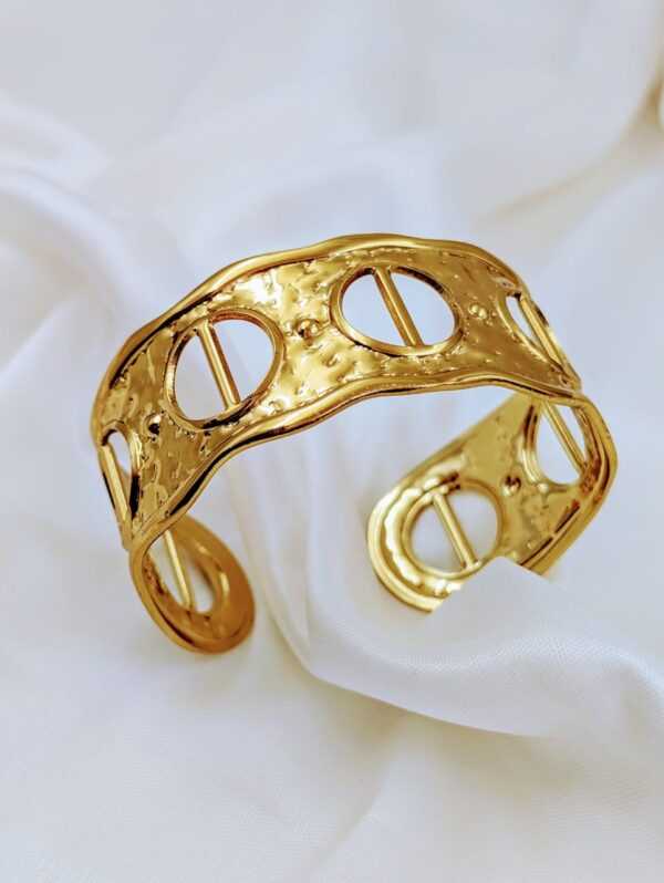Close-up of a golden textured bracelet with circular and bar design elements, by Jhunkaar.