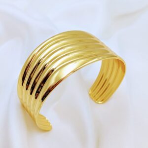 Golden layered cuff bracelet by Jhunkaar on a white silk background.
