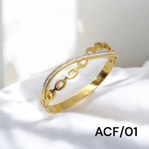 Gold bangle bracelet with open oval link design and a curved line of embedded stones, displayed on a white fabric background.