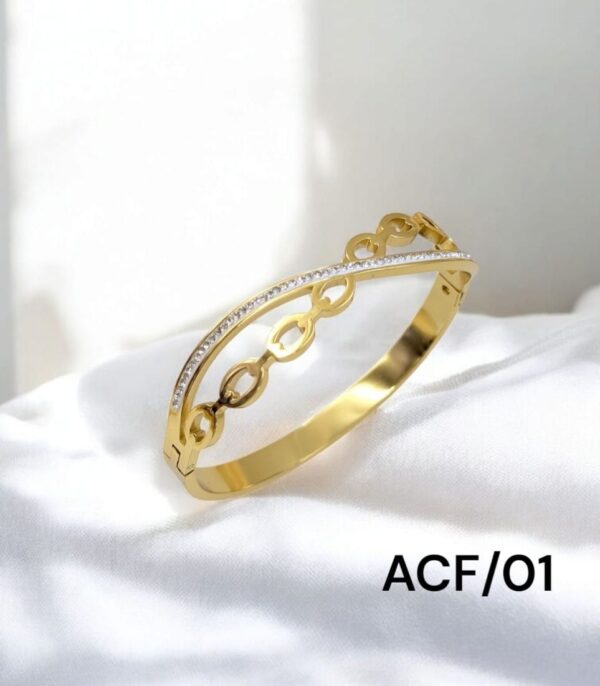 Gold bangle bracelet with open oval link design and a curved line of embedded stones, displayed on a white fabric background.